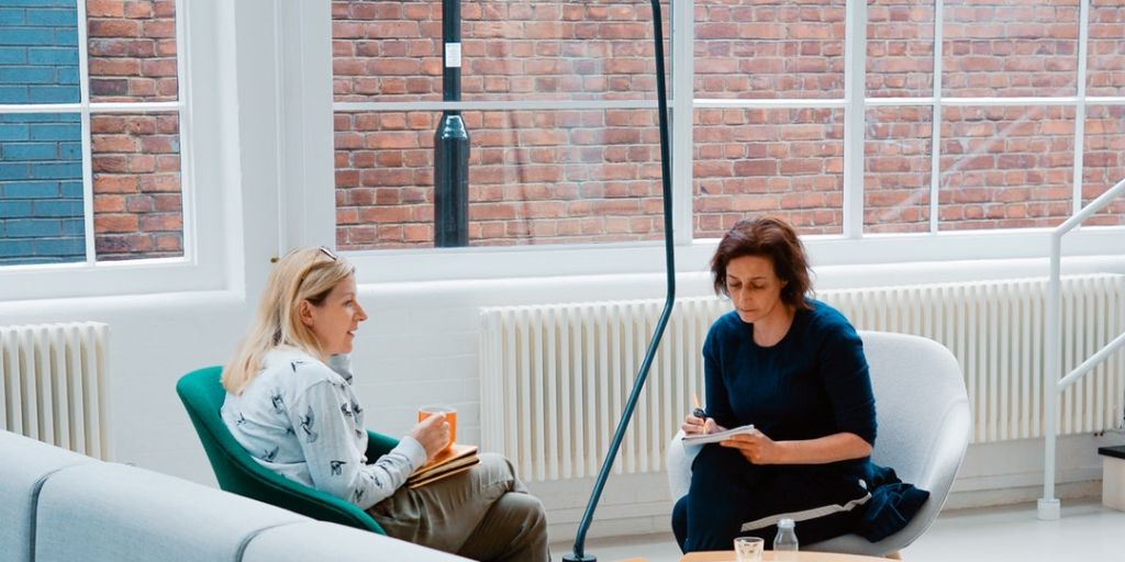 5 Surprising Ways Counseling Can Help Two women sitting in chairs in front of a wall windows talking