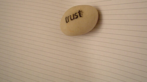 A small stone engraved with the word trust sitting on a lined paper